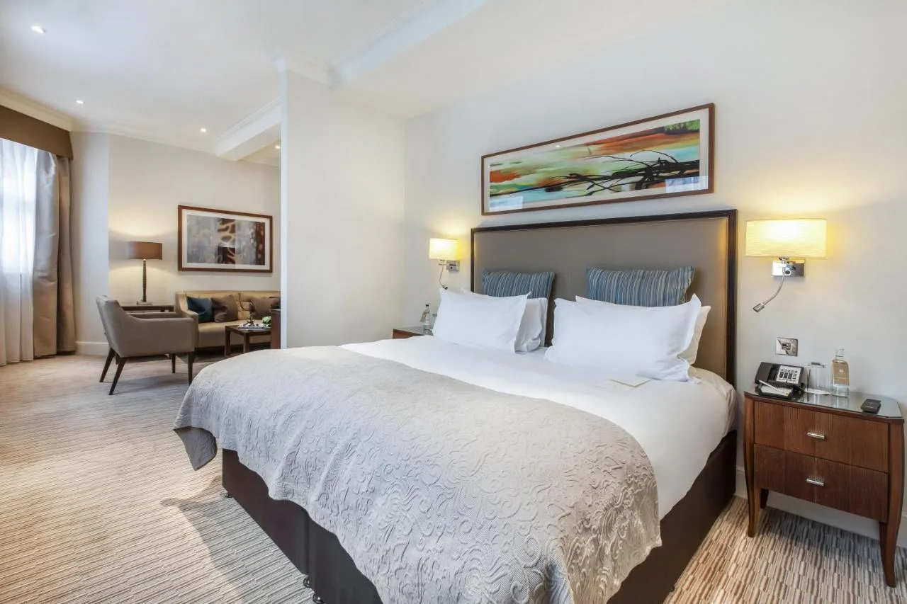 Hotel room with a large bed and armchair at St. James' Court, A Taj Hotel, London